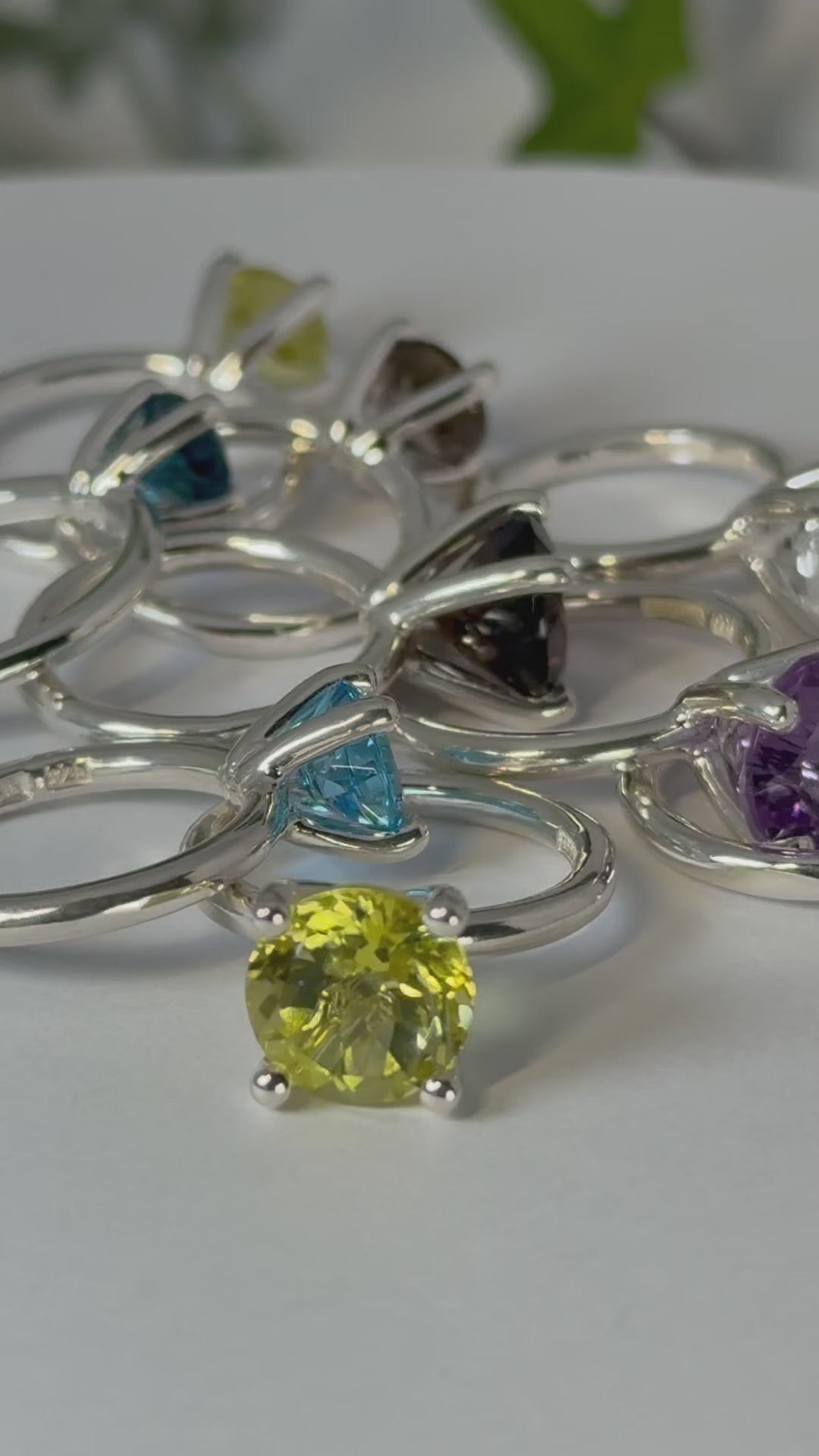 Ringar Candy i silver med stenar i olika färger som gul, blå, brun och lila som ligger på en bricka som snurrar.